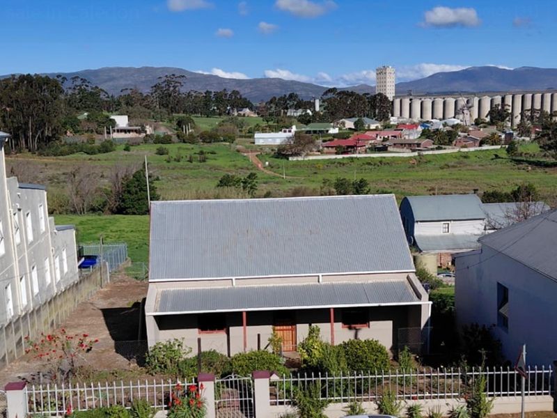 Aerial view of a residential property featuring a corrugated metal roof, front veranda, and perimeter fencing, set within a rural town landscape.