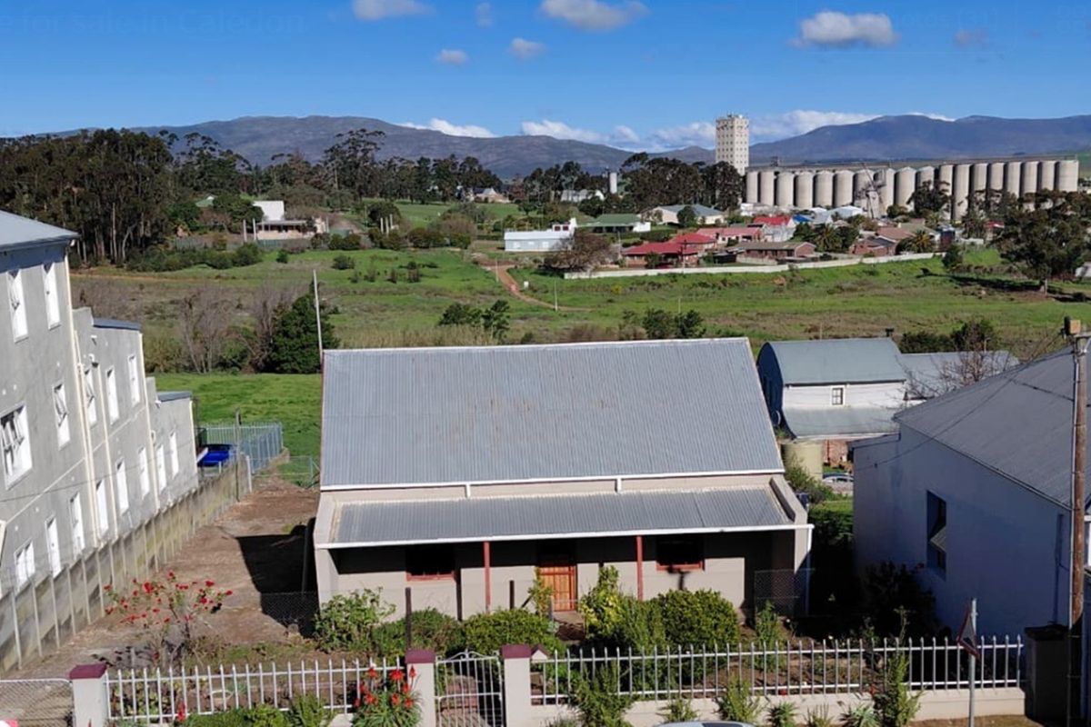 Aerial view of a residential property featuring a corrugated metal roof, front veranda, and perimeter fencing, set within a rural town landscape.