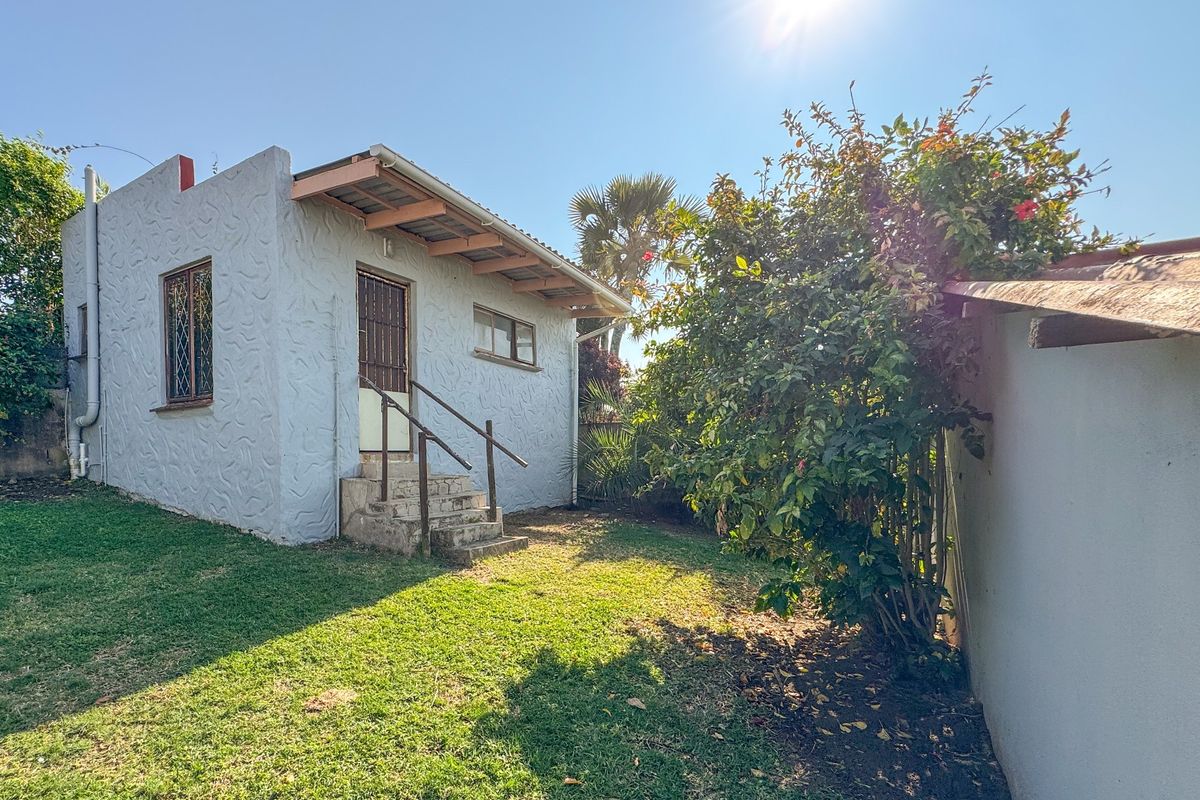 Rear view of the property featuring a textured facade, concrete entrance steps with a metal handrail, and security bars on the windows.