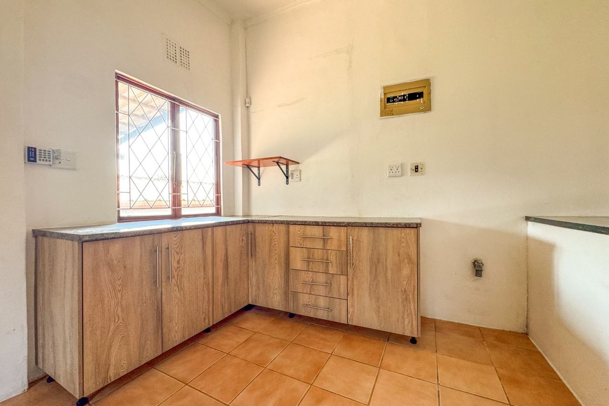 A functional, empty kitchen area featuring wood-look laminate cabinetry, stone-effect countertops, and ceramic floor tiles, ready for personalization or modern updates.
