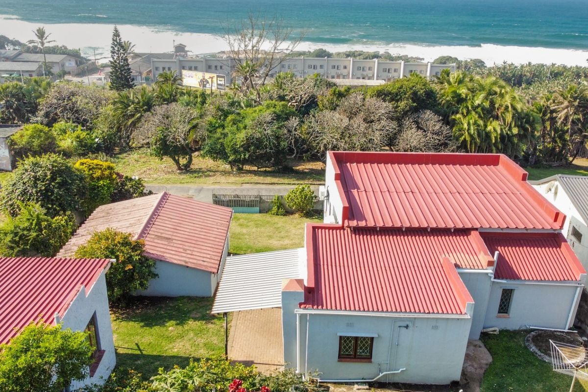 Aerial view of the property showing the main house, detached garage, paved patio area, and surrounding garden with coastal views in the background.