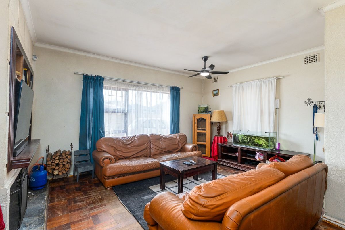 A living room featuring parquet flooring, a ceiling fan, and a fireplace, offering a comfortable space with potential for cosmetic updates.