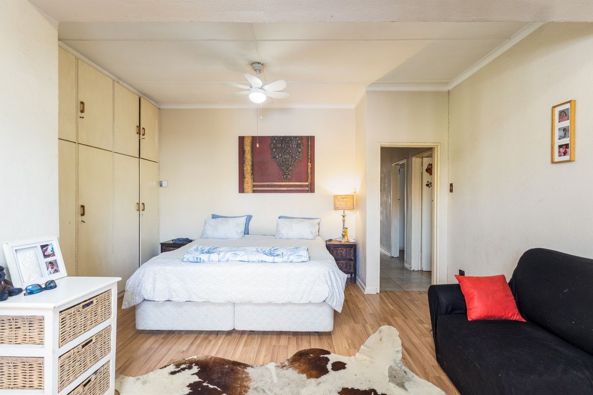 A bedroom featuring laminate flooring, built-in cupboards, and a ceiling fan, offering a functional space with potential for modern updates.