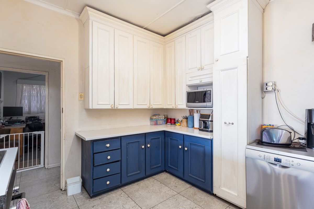 A functional kitchen featuring two-tone cabinetry, laminate countertops, and a built-in microwave, with tiled flooring and a tall pantry storage unit.