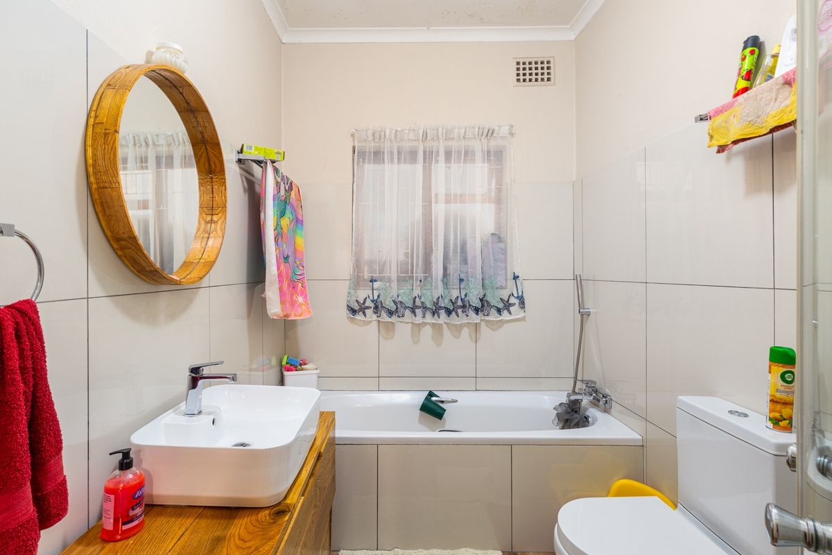 A functional bathroom featuring a vessel sink on a wooden vanity, a built-in bathtub, and neutral wall tiling.