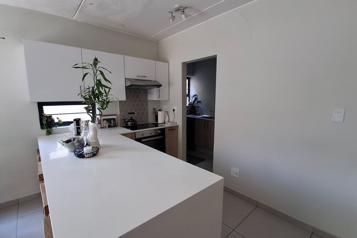 Modern kitchen featuring a central island, built-in oven, hob, extractor fan, and tiled backsplash, with an adjacent scullery area.