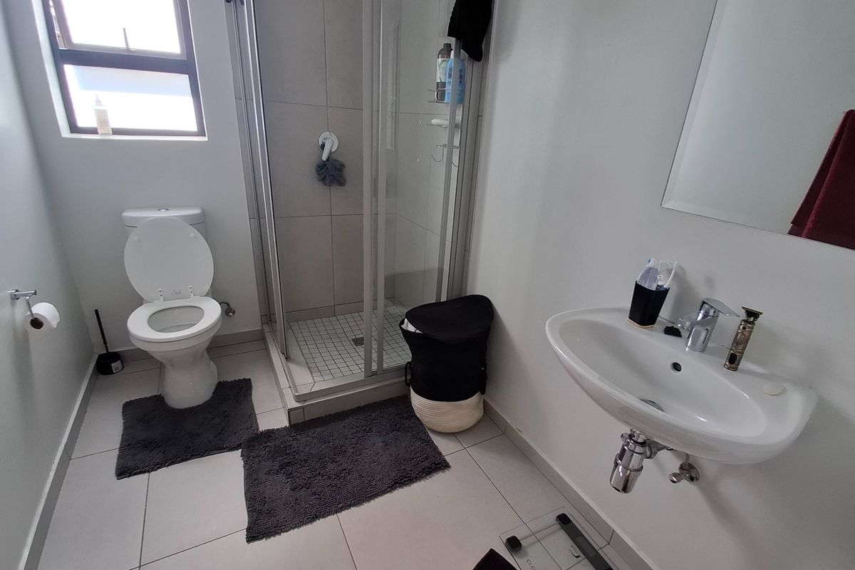 A functional bathroom featuring a shower enclosure, wall-mounted basin, and toilet with neutral tiled flooring and finishes.