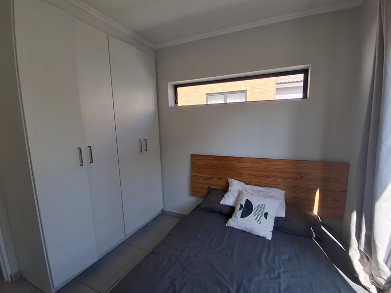 A modern bedroom featuring built-in cupboards, tiled flooring, and a horizontal clerestory window providing natural light.