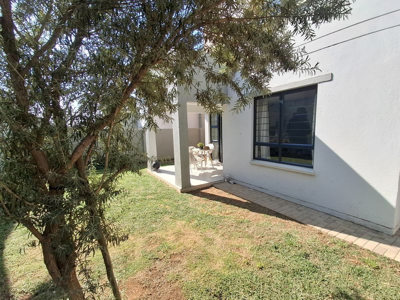 A view of the rear exterior featuring a covered patio, paved walkway, and a well-maintained lawn area.
