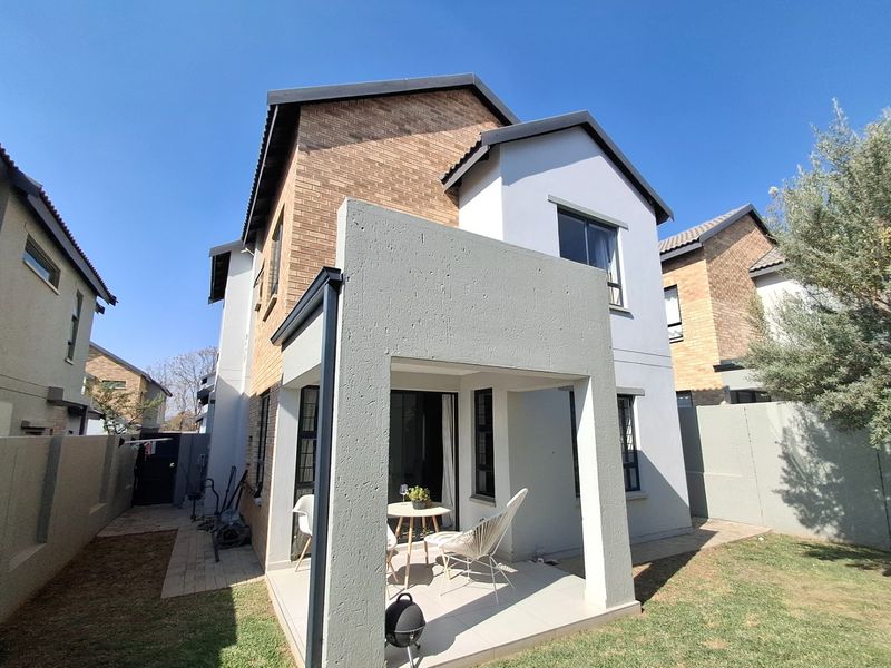 Rear view of a two-story residential house featuring a covered patio, brick and plastered exterior finishes, and a private garden area.