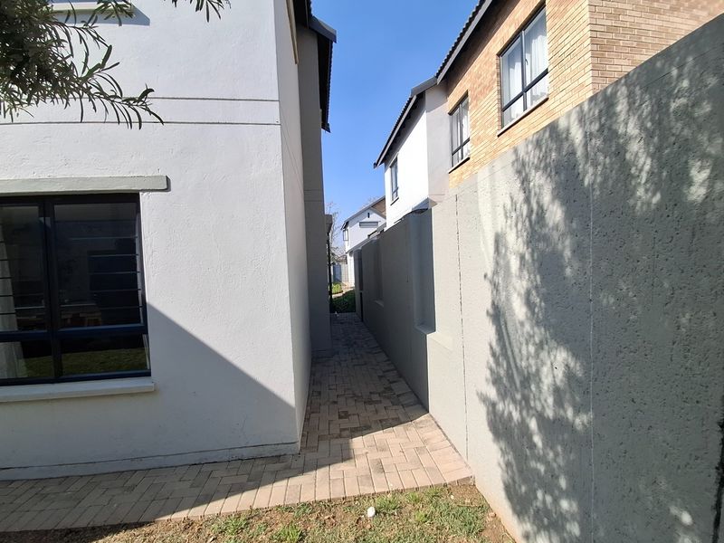 A narrow paved side passage between the main house structure and the boundary wall, featuring clean exterior finishes and aluminium window frames.