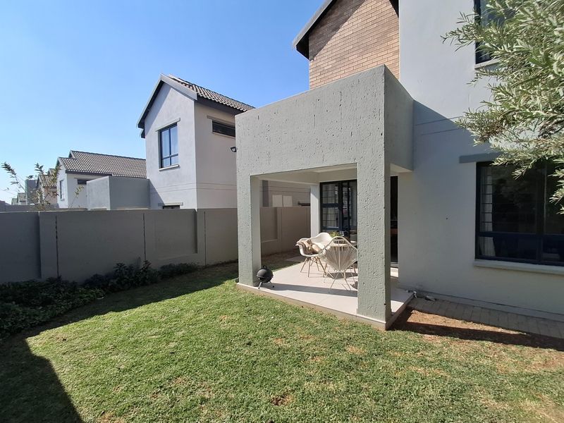 Rear view of the property featuring a covered patio area, tiled flooring, and a private garden with boundary walls.