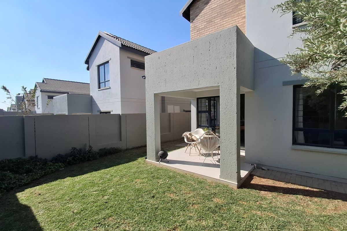 Rear view of the property featuring a covered patio area, tiled flooring, and a private garden with boundary walls.