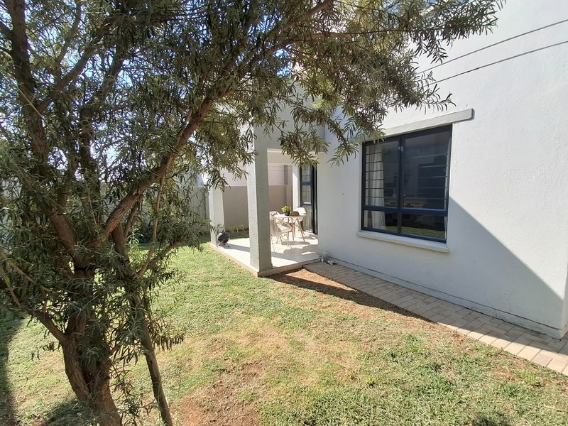 A view of the rear exterior featuring a covered patio, paved walkway, and a well-maintained garden area with established trees.
