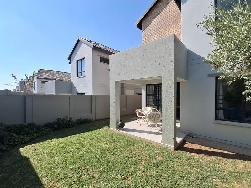 A rear view of the property featuring a covered patio area with tiled flooring, overlooking a private garden with a boundary wall.
