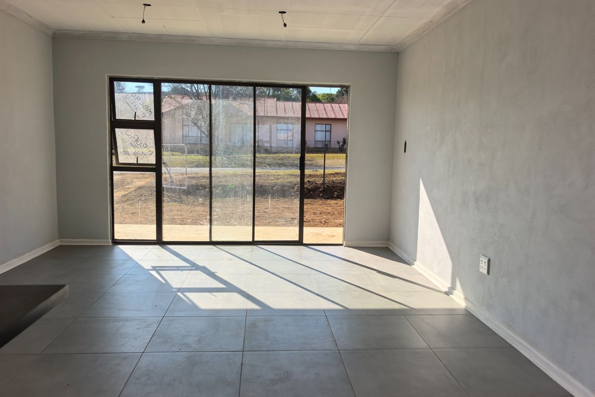 An empty, unfinished living room featuring large sliding glass doors, tiled flooring, and neutral wall finishes, ready for final touches.