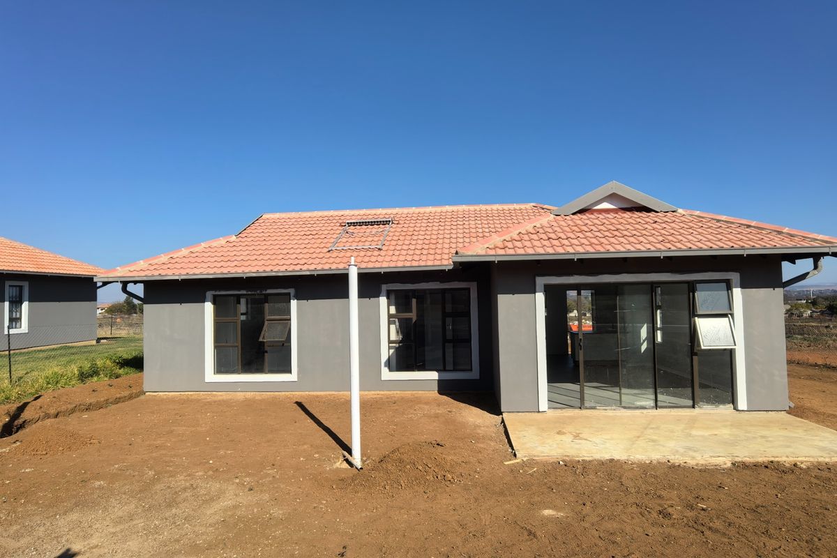 Rear view of a modern house featuring a tiled roof with solar water heater, aluminium windows, and a concrete patio area with unfinished landscaping.