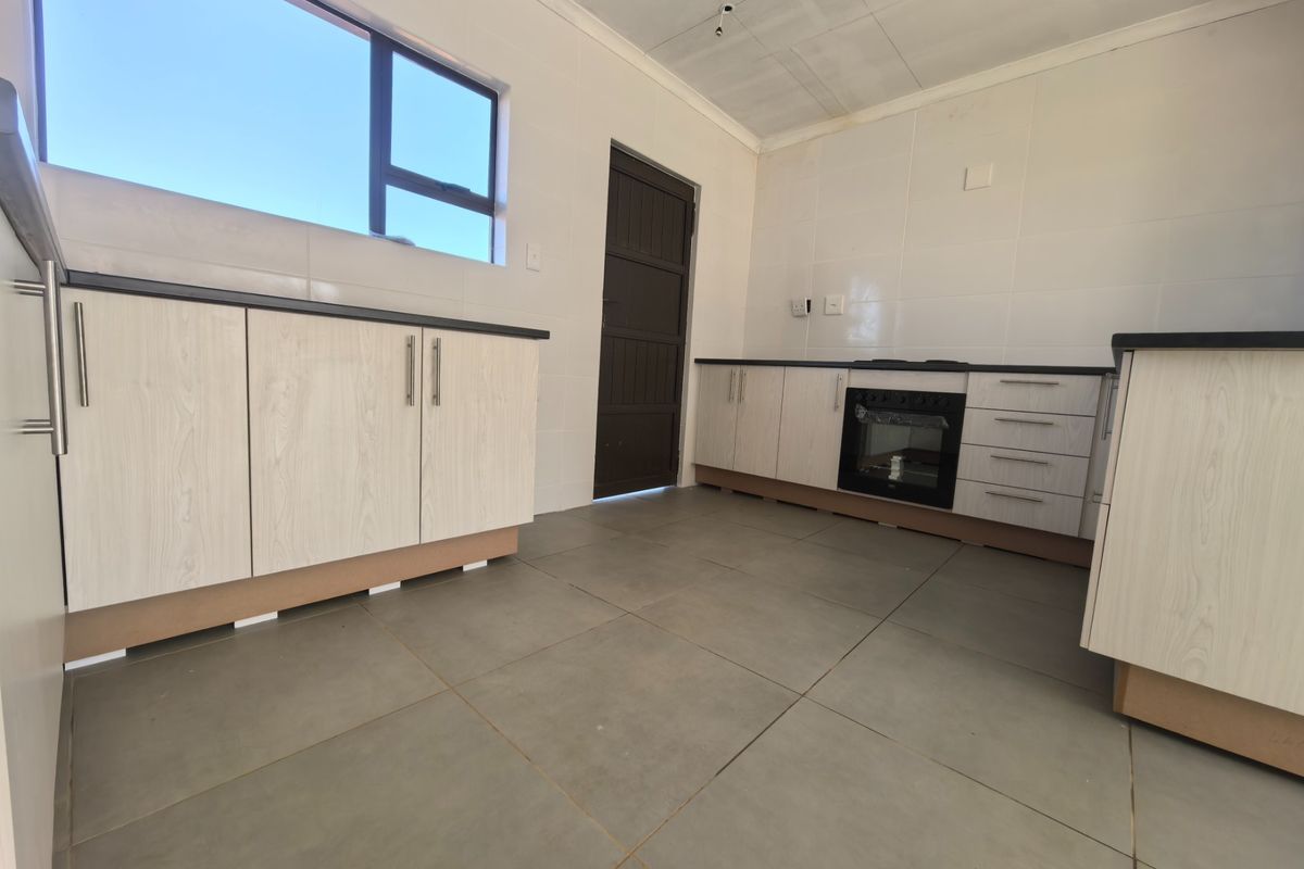 An unfinished kitchen featuring light wood-grain cabinetry, dark countertops, built-in oven, and large format floor tiles, requiring final touches to complete the installation.
