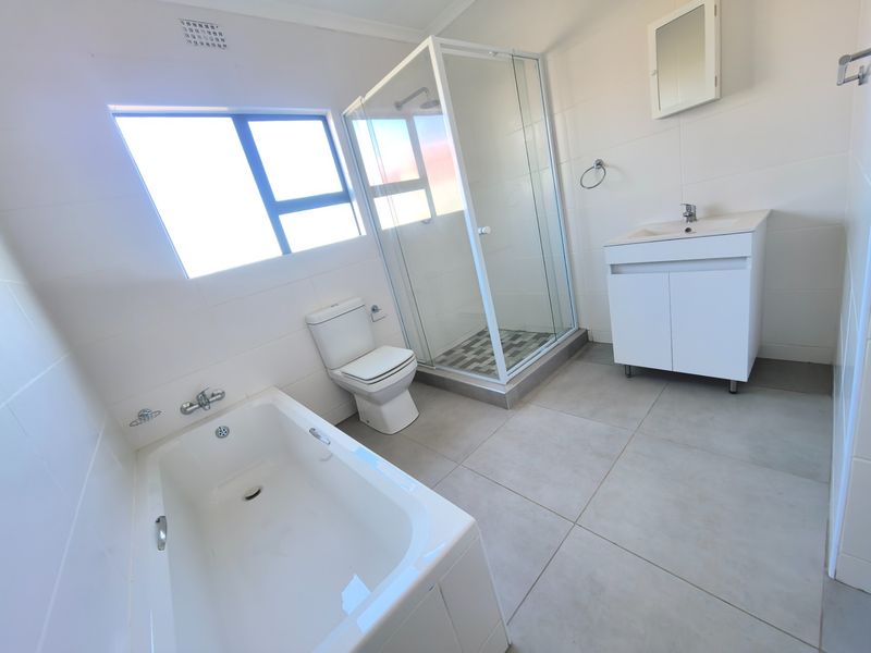 A clean, modern bathroom featuring a separate shower enclosure, bathtub, vanity cabinet, and neutral wall and floor tiling.