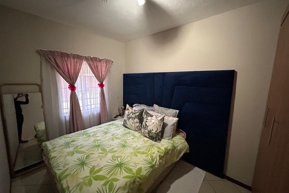 A bedroom featuring tiled flooring and a window fitted with security bars. The room includes an exposed ceiling light fixture.