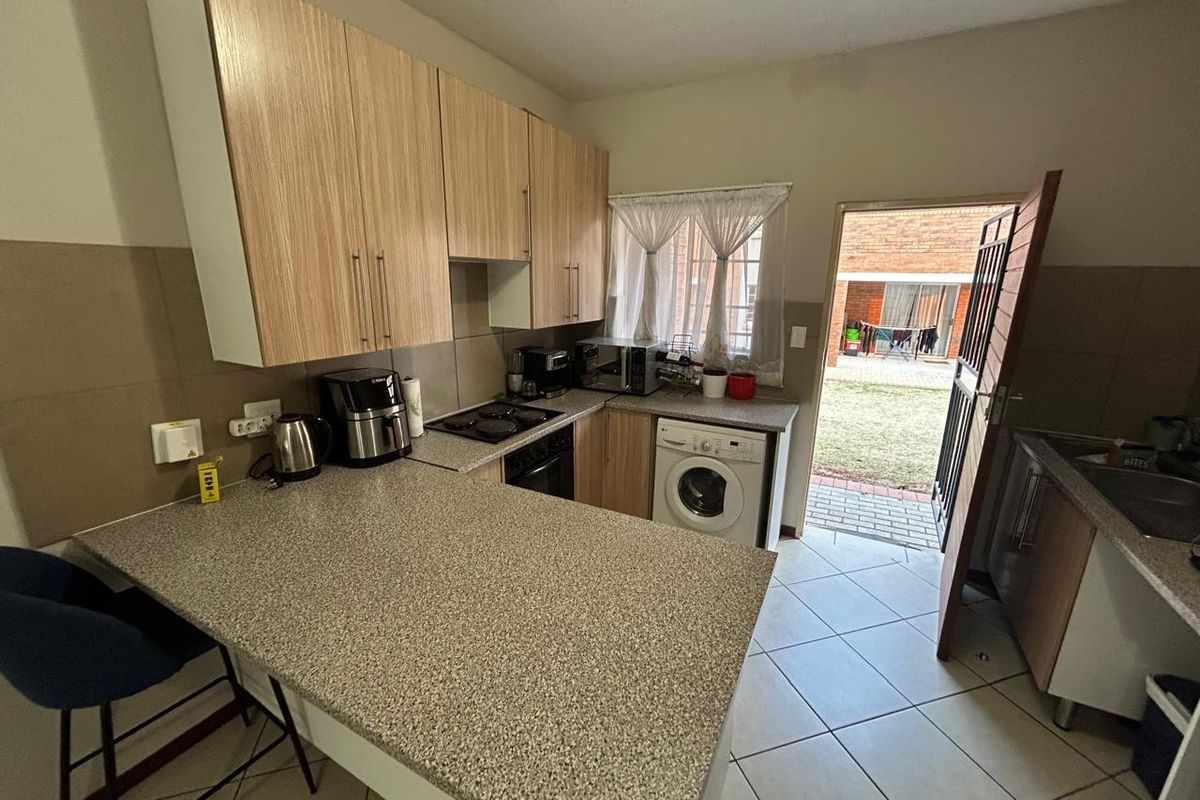Functional kitchen featuring laminate cabinetry, granite-look countertops, built-in oven, electric hob, and integrated washing machine, with direct access to the rear garden.