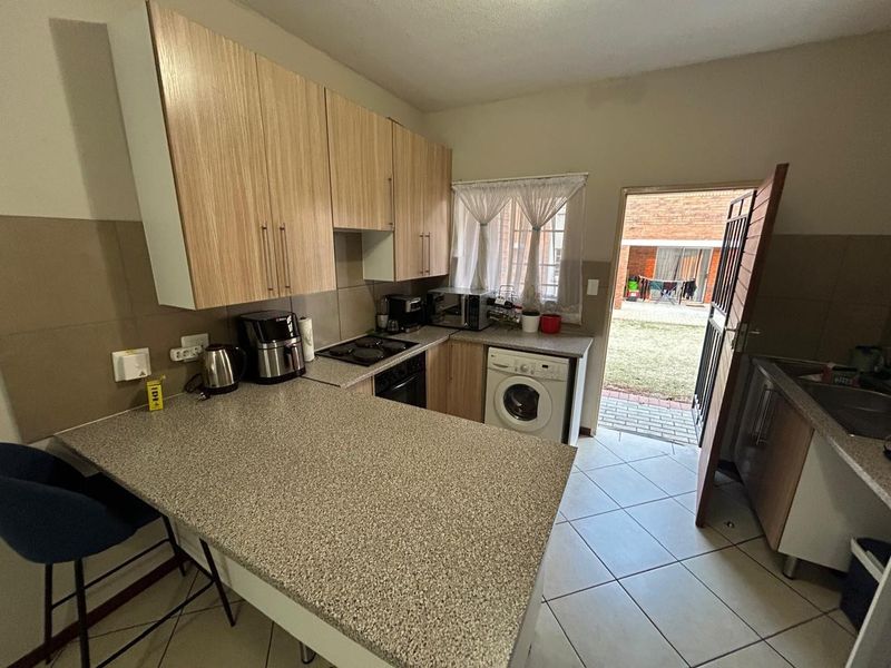 Functional kitchen featuring laminate cabinetry, granite-look countertops, built-in oven, electric hob, and integrated washing machine, with direct access to the rear garden.