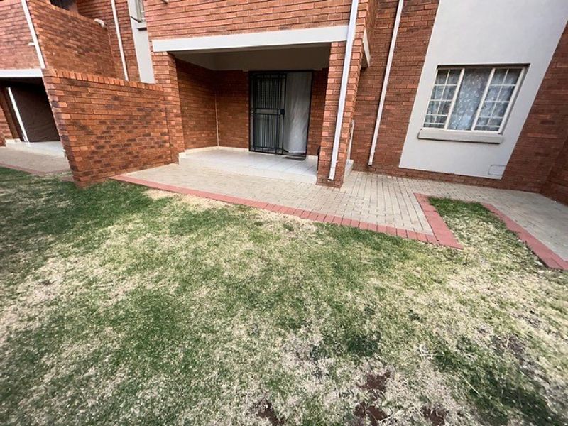 A rear view of the apartment featuring a brick facade, a paved patio area, and a small private garden space.