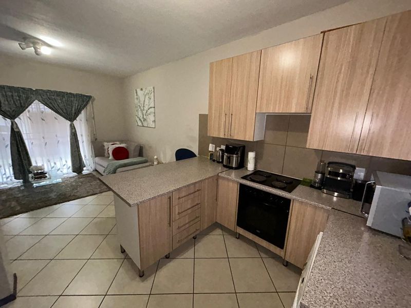 Open-plan living area featuring a functional kitchen with wood-finish cabinetry, electric hob, oven, and tiled flooring, leading to a bright living space.