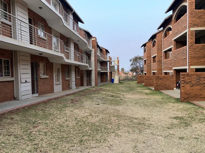 View of the apartment complex exterior featuring face brick facades, metal balcony railings, and a shared communal lawn area between the buildings.