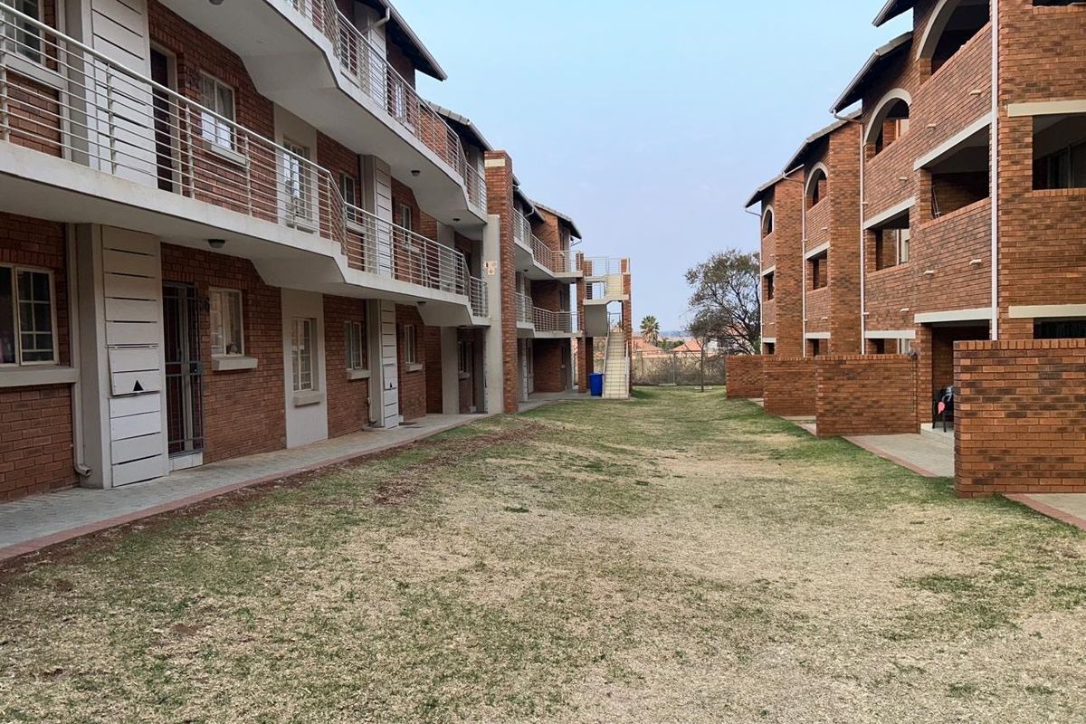 View of the apartment complex exterior featuring face brick facades, metal balcony railings, and a shared communal lawn area between the buildings.