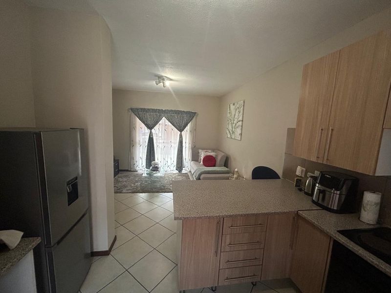 Open-plan living area featuring a functional kitchen with laminate cabinetry and tiled flooring, seamlessly flowing into a comfortable lounge space with balcony access.