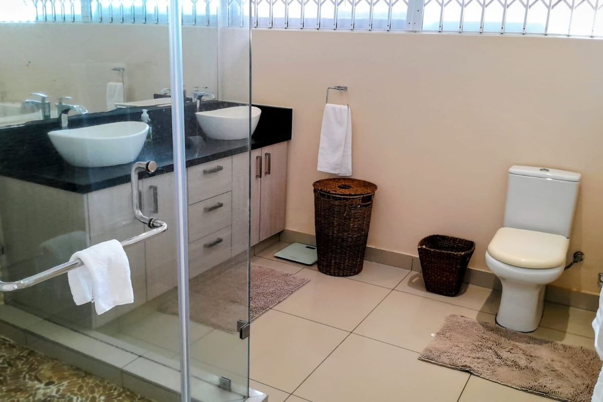 A well-maintained bathroom featuring a double vanity with vessel sinks, granite countertops, and a glass-enclosed shower.