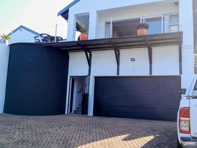Front elevation of a two-story house featuring a paved driveway, double garage, and an upper-level balcony with modern finishes.