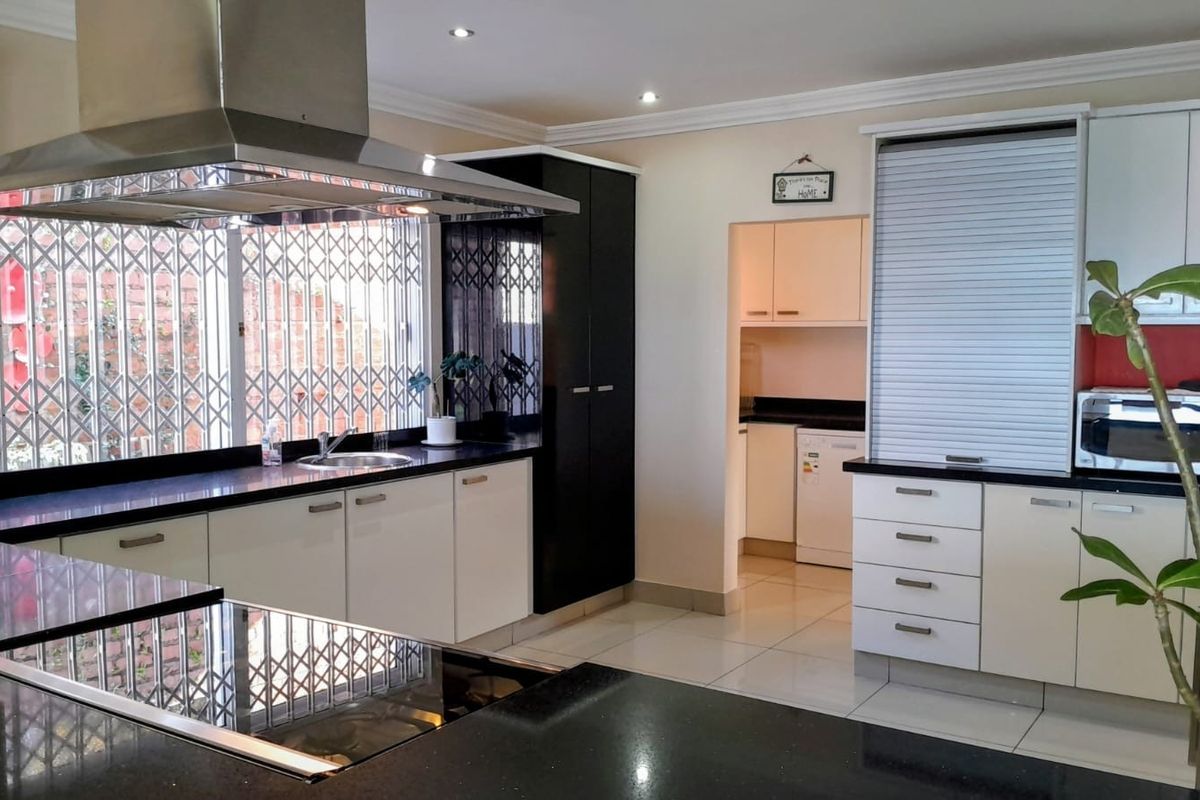Modern kitchen featuring sleek white and black cabinetry, granite countertops, a stainless steel extractor fan, and a convenient appliance garage.