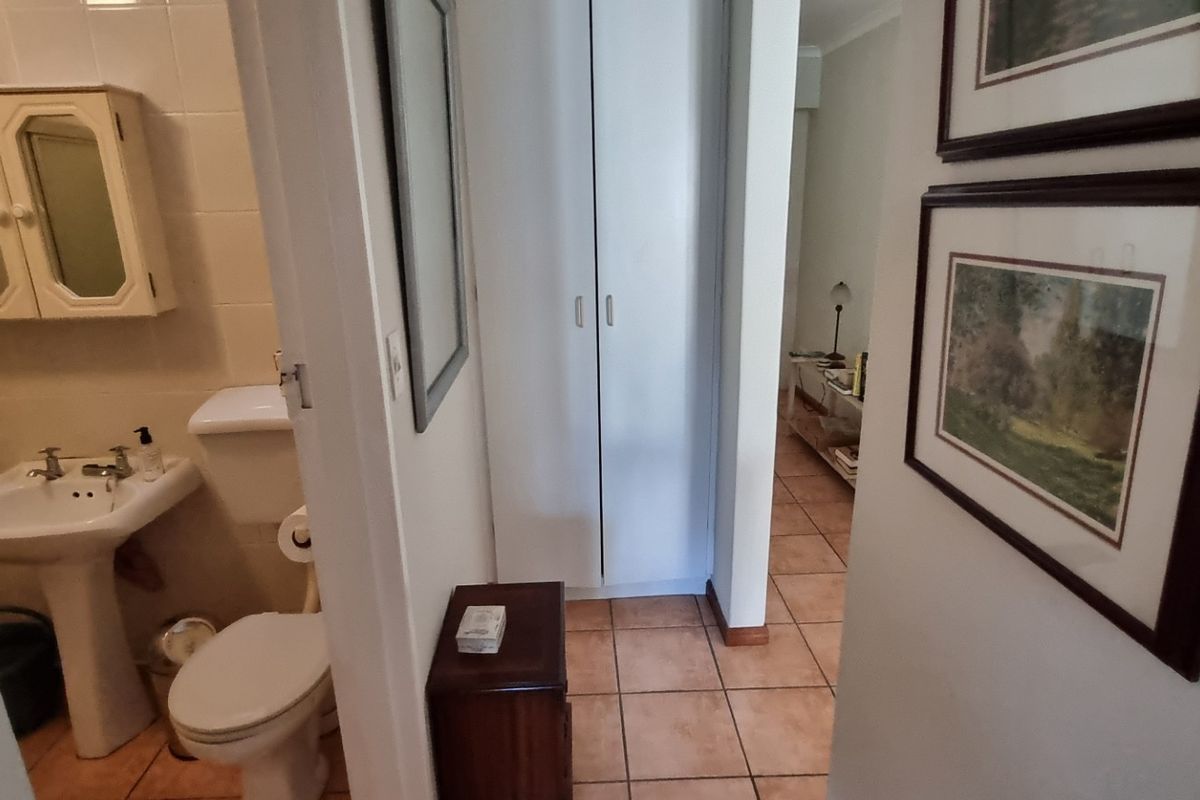 A functional bathroom featuring a pedestal sink, toilet, and built-in storage, connected to a hallway with tiled flooring and built-in cupboards.