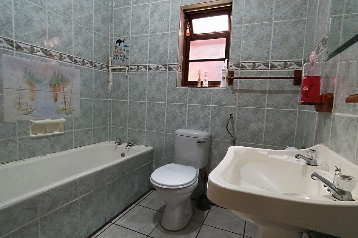 A functional bathroom featuring a bathtub, pedestal sink, and toilet with full-height wall tiling and a small casement window.