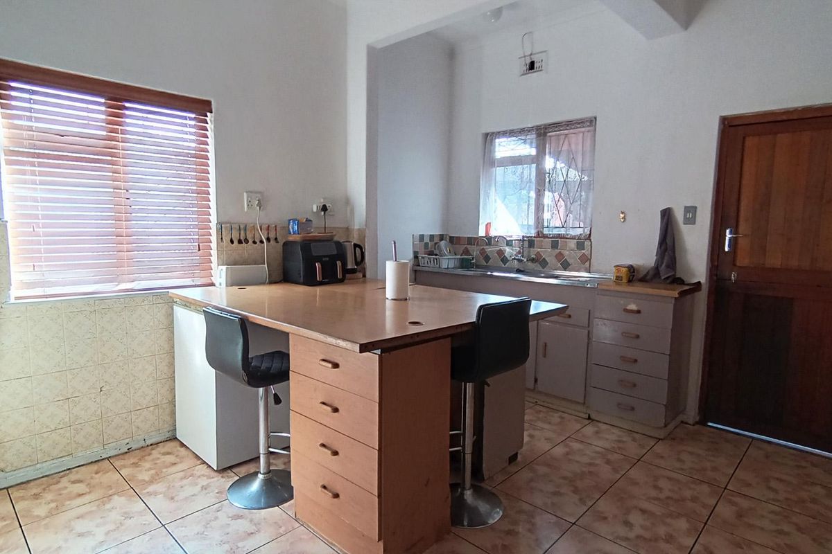 A functional kitchen featuring a central island, tiled splashbacks, built-in cabinetry, and tiled flooring with direct access to an exterior door.