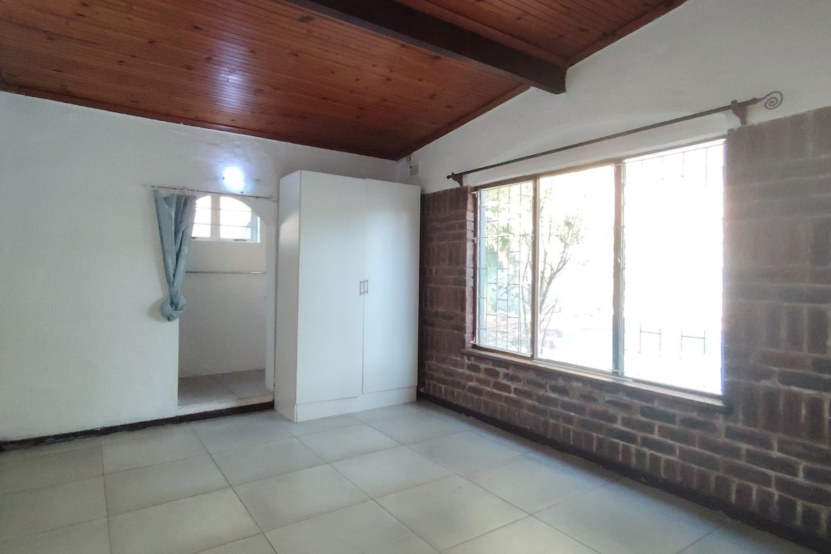A bedroom featuring an exposed timber ceiling, exposed brick feature wall, tiled flooring, and a built-in wardrobe.