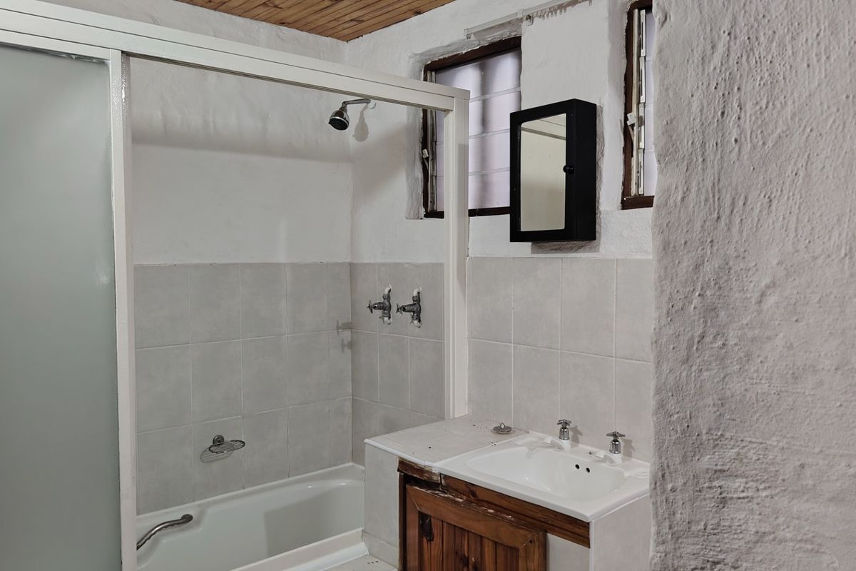 A dated bathroom featuring a shower-over-bath combination, a vanity unit with a washbasin, and a timber-clad ceiling.