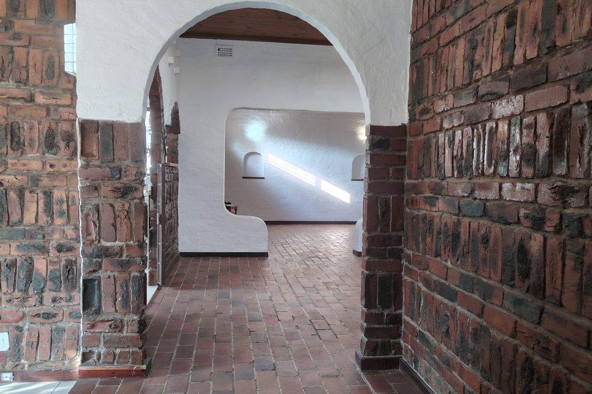 Spacious interior area featuring distinctive exposed brick walls, arched architectural transitions, and terracotta tile flooring, offering a unique rustic aesthetic.