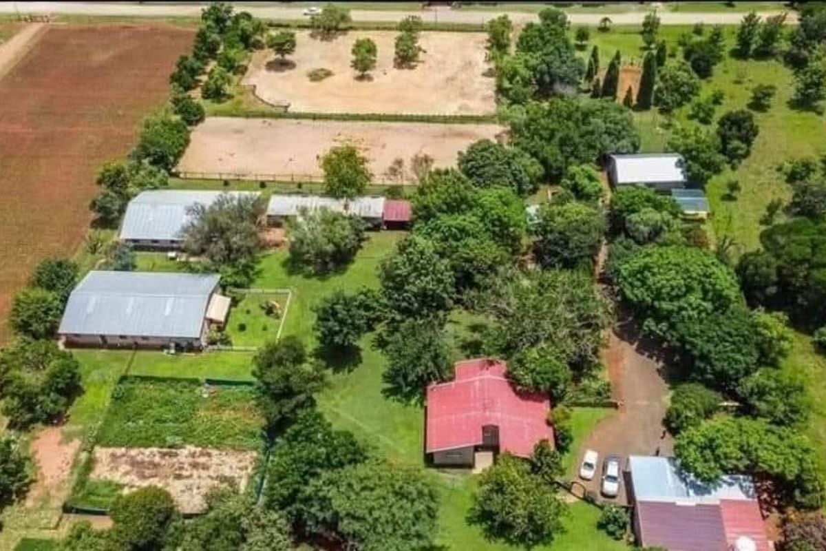 Aerial view of a farm property featuring multiple outbuildings, metal-roofed structures, fenced paddocks, and established landscaping on a large rural plot.