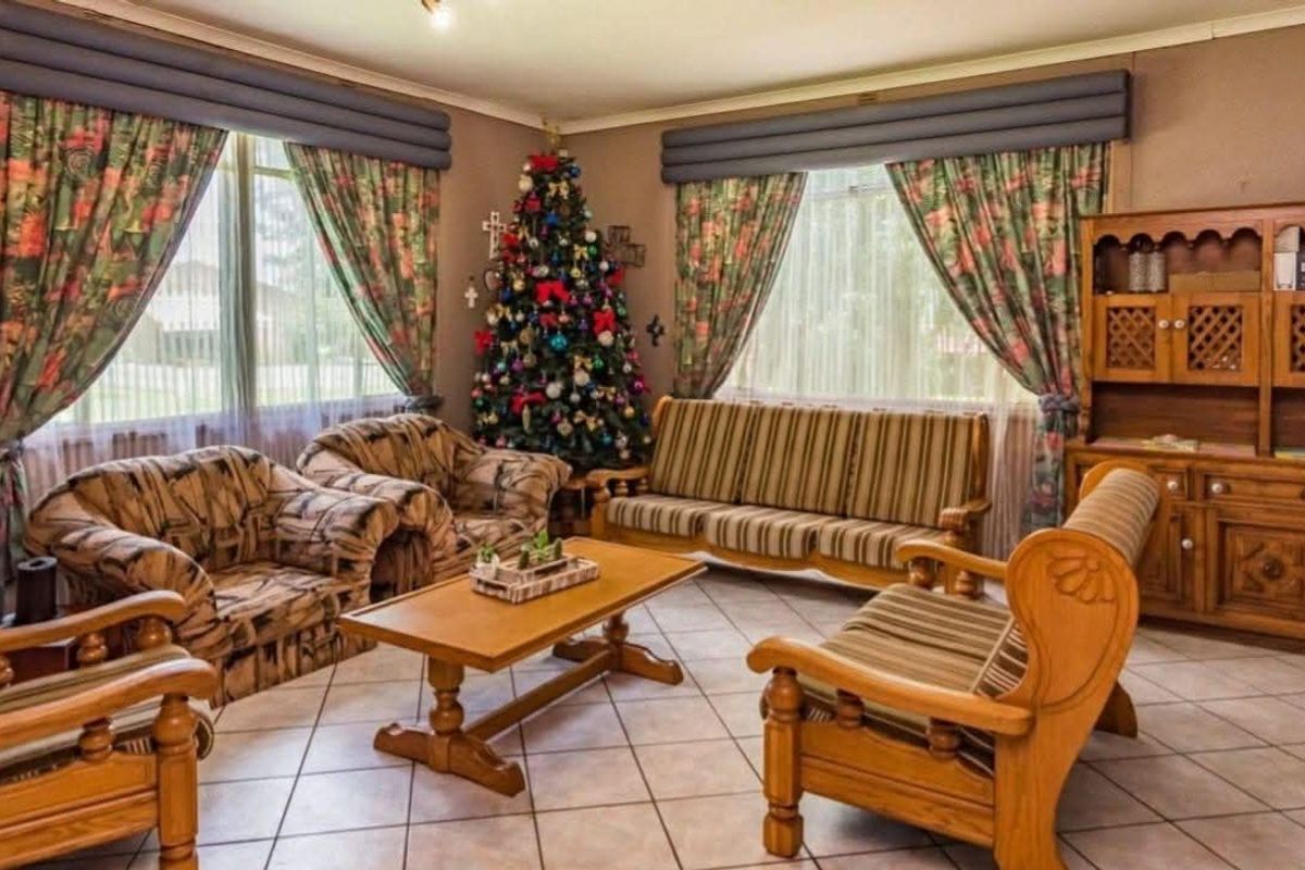 A spacious living room featuring neutral tiled flooring and large windows with built-in pelmets, offering a comfortable and traditional living space.