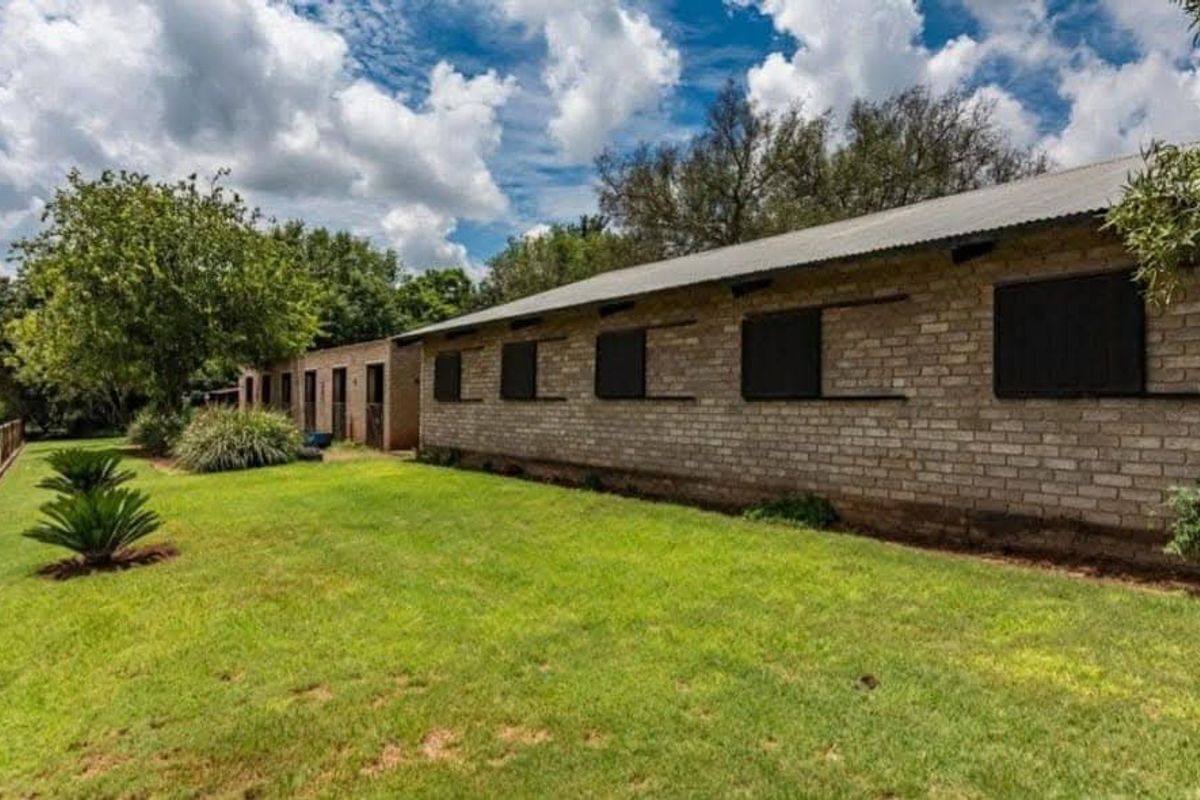 Exterior view of a brick farm building featuring a corrugated metal roof and stable-style access doors, set within a well-maintained garden area.
