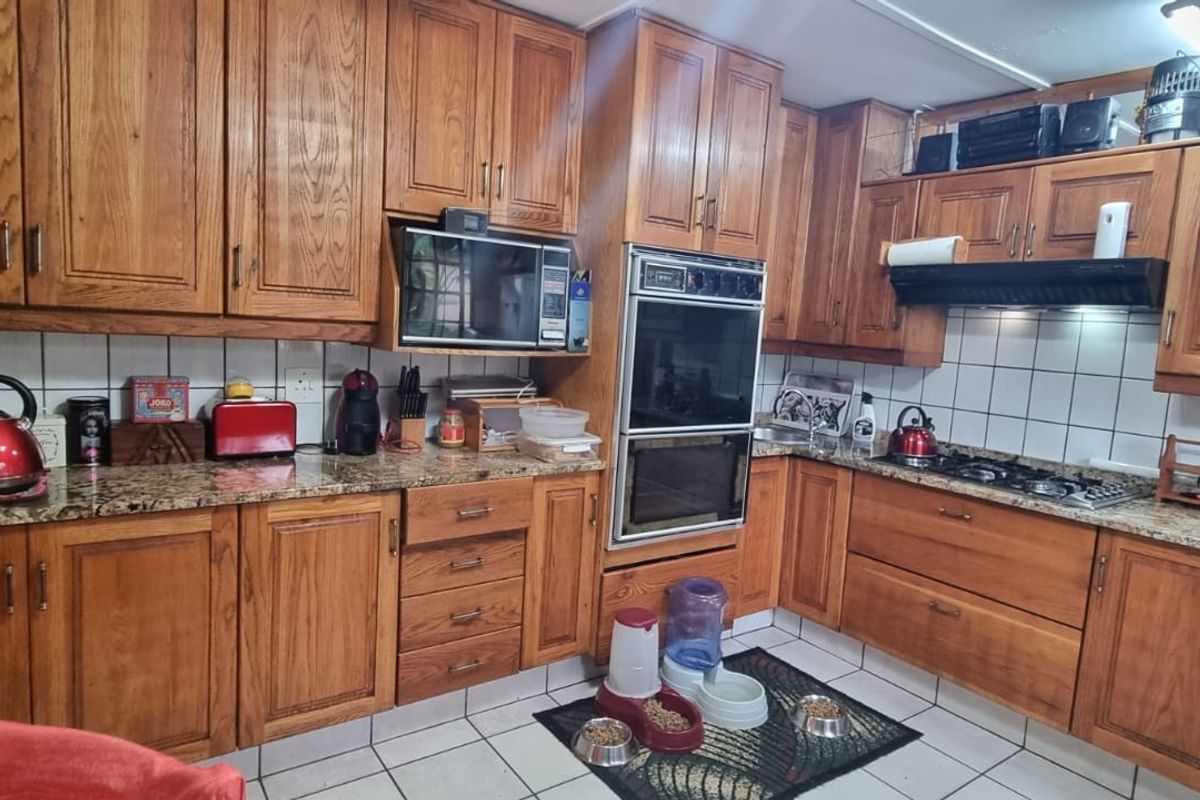 A functional kitchen featuring traditional wooden cabinetry, granite countertops, a built-in double oven, and a gas hob with an extractor fan.