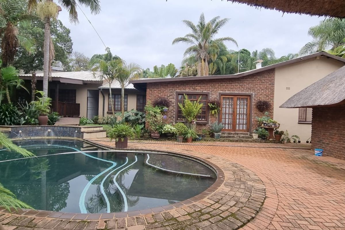 Rear exterior view of a farm-style property featuring a swimming pool, brick paved patio area, and traditional thatched roof architecture.