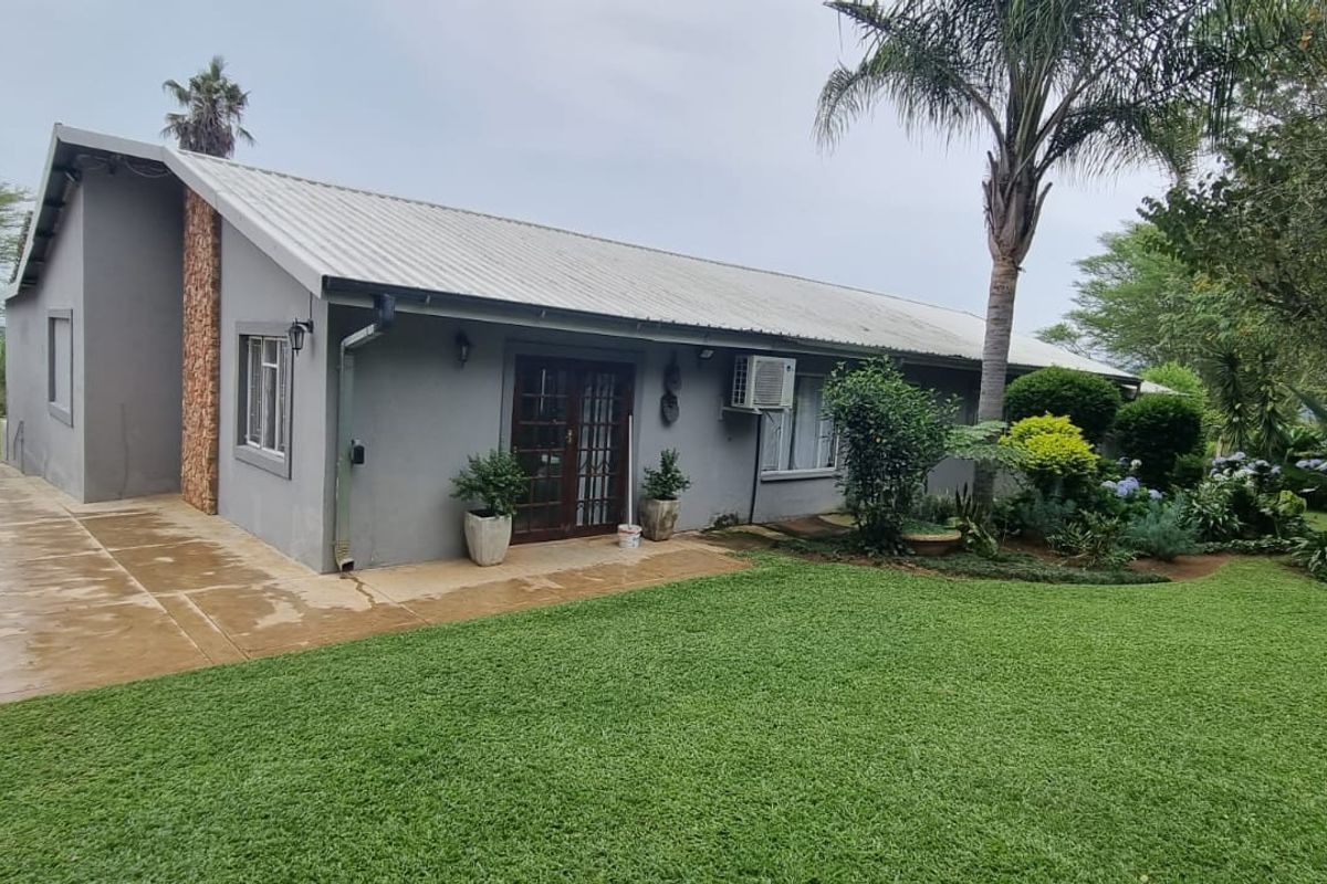 Rear view of the farm dwelling featuring a corrugated metal roof, stone accent wall, concrete driveway, and established garden surroundings.