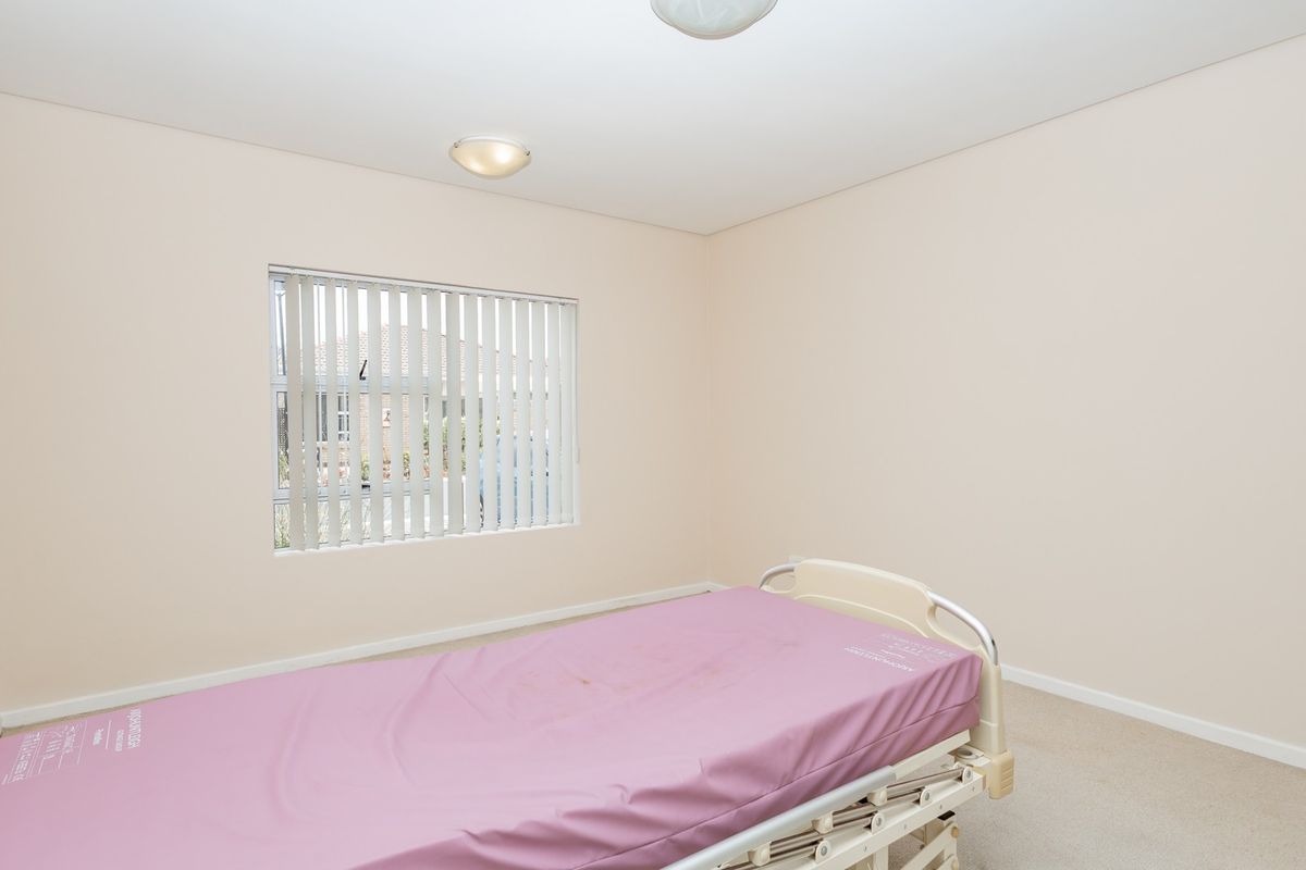 A neutral-toned bedroom featuring carpet flooring, vertical window blinds, and dual ceiling light fixtures.
