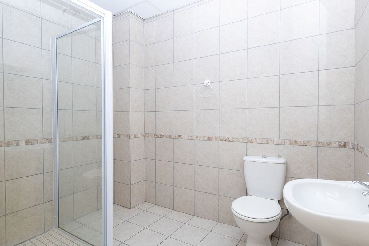 A clean, functional bathroom featuring a glass-enclosed shower, pedestal washbasin, and neutral ceramic tiling throughout.