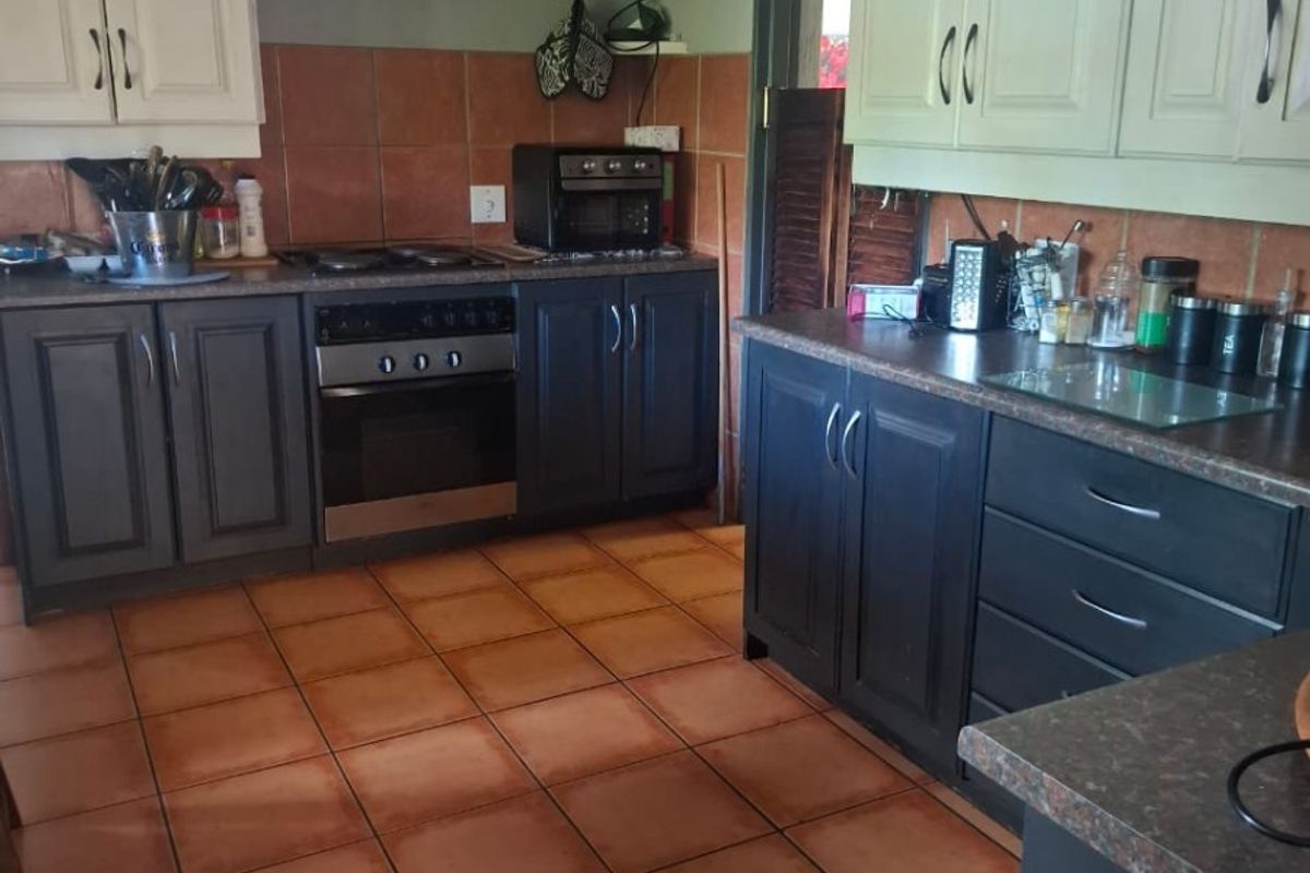 A functional kitchen featuring two-tone cabinetry, built-in oven and hob, tiled backsplash, and terracotta-style floor tiles.