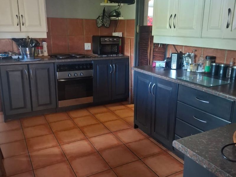 A functional kitchen featuring two-tone cabinetry, built-in oven and hob, tiled backsplash, and terracotta-style floor tiles.